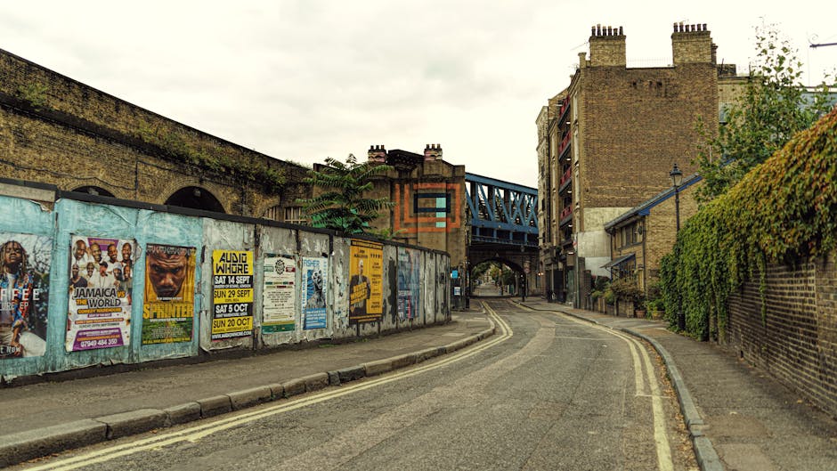 A straight residential street on Blackstock Road in Finsbury Park, featuring a paved roadway scattered with fallen leaves, flanked by modern multi-storey office or apartment buildings on the right sid